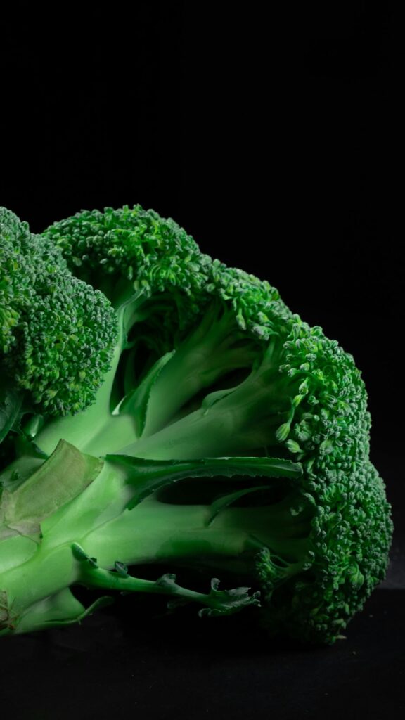 Close-up of fresh green broccoli against a black background, highlighting its texture. Broccoli is helpful in eating with endometriosis