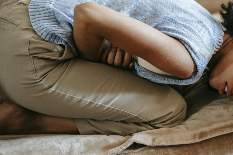 A young woman in discomfort, holding her stomach while curled up on a couch indoors.