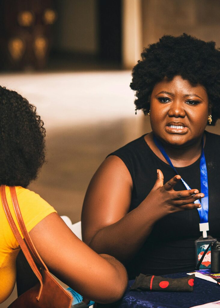 Two African women in conversation outside, expressing with hand gestures.