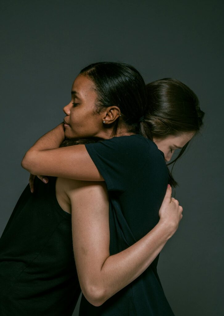 Two women share a comforting hug symbolizing empathy and support in a studio setting.