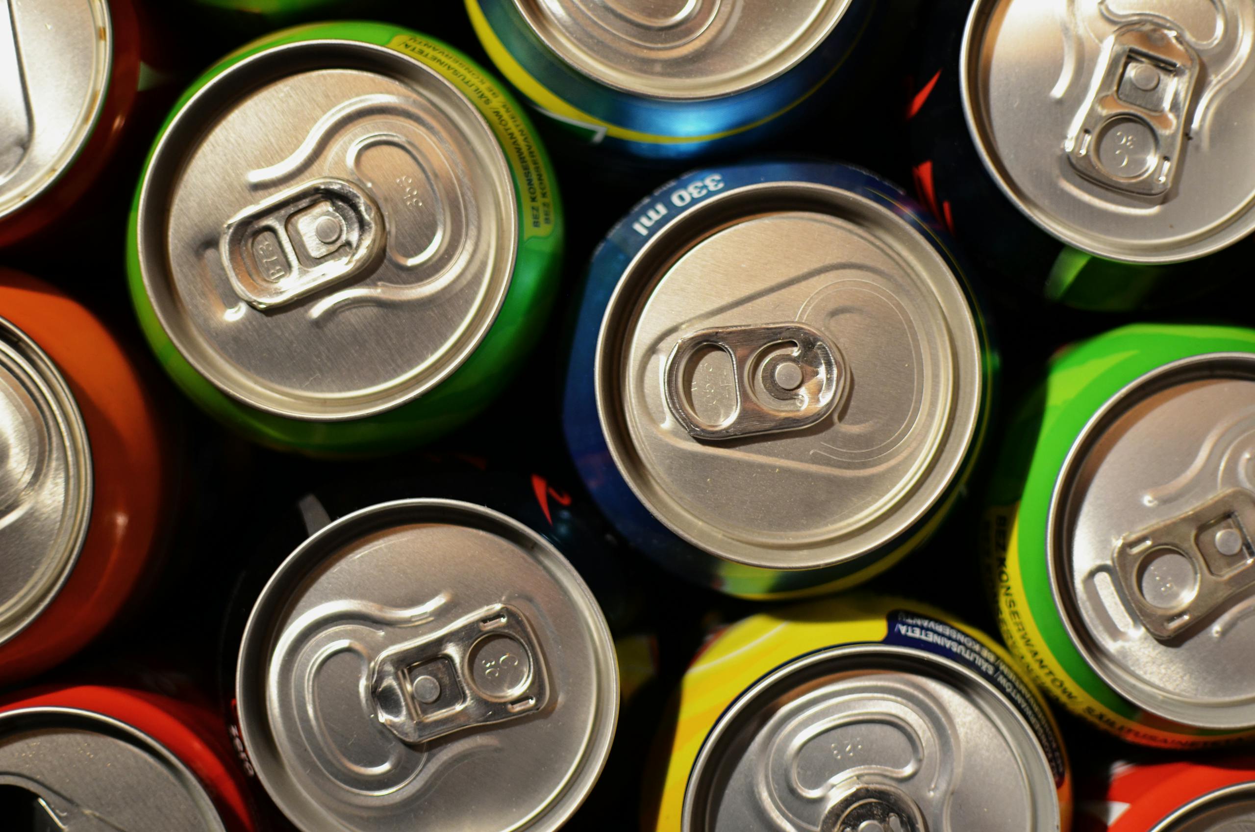 Close-up of colorful beverage cans arranged closely together, showcasing various colors. Sugary drinks